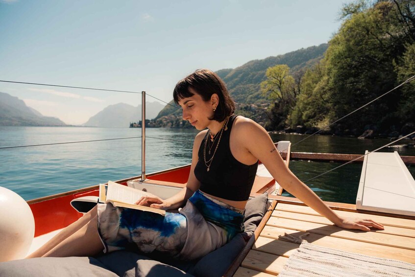 A person reading a book on a boat with a lake and mountains in the background. 5
