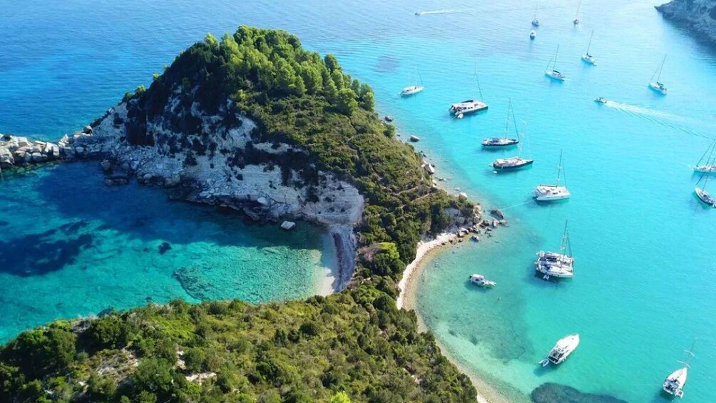 A coastal landscape with a prominent rocky island surrounded by clear turquoise waters, several boats anchored near the shore, and lush greenery. 3