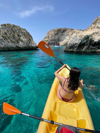 A person kayaking in clear turquoise water with rocky cliffs in the background. 3