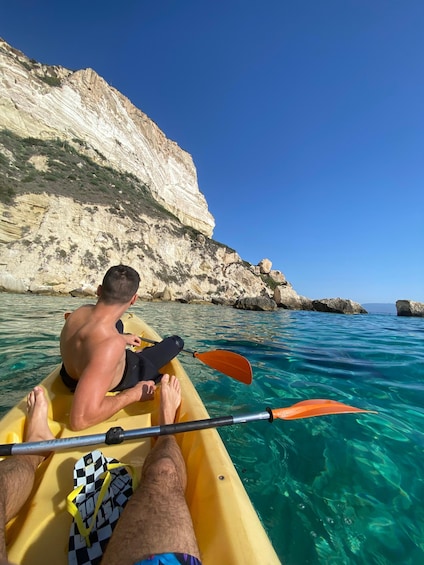 A person kayaking on clear turquoise water with a rocky cliff in the background. 1