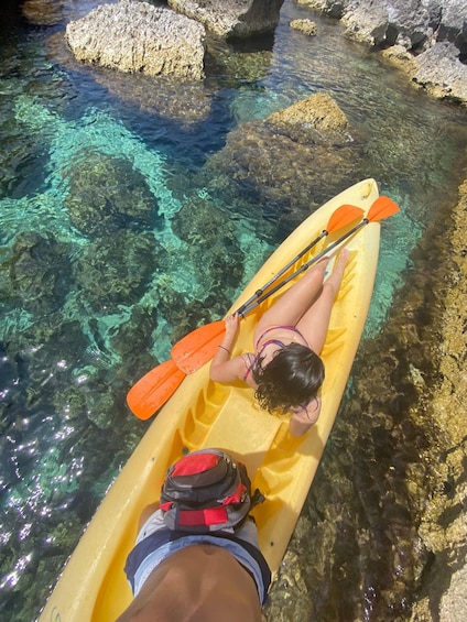 A person kayaking on a clear river with visible rocks and aquatic plants. 2
