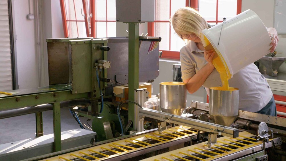 A person pouring a yellow liquid into a stainless steel container on a production line. 2