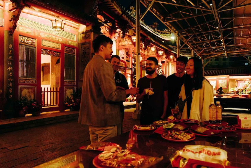 A group of people dining outdoors at night in a traditional setting with ornate architecture. 1