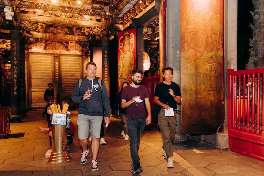 A group of people walking through a temple with ornate decorations and Chinese characters on the walls. 2