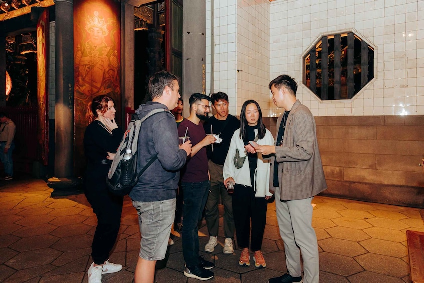 A group of people standing and conversing in an urban setting with tiled walls and a decorative column. 4