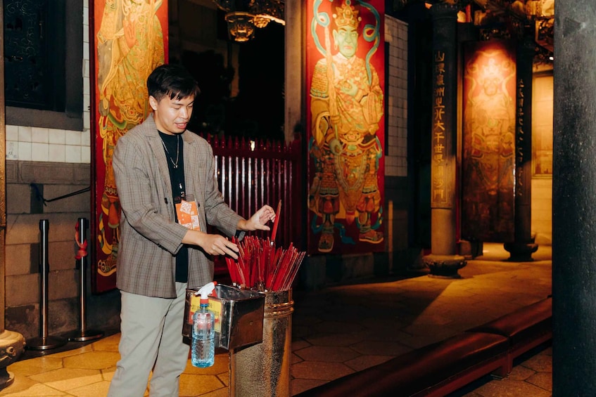 A person lighting incense sticks in a temple with traditional Chinese murals. 5