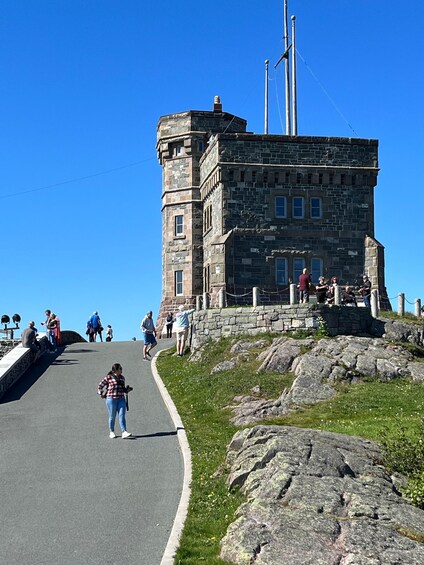 A stone building with a tower, a paved road, and people walking. 1