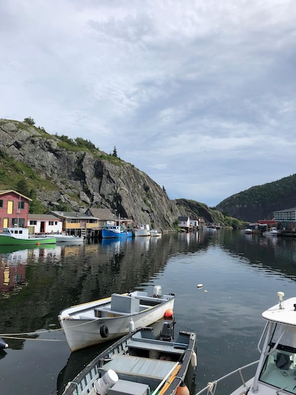 A calm harbor with boats docked, a rocky cliff, and buildings along the water's edge. 5