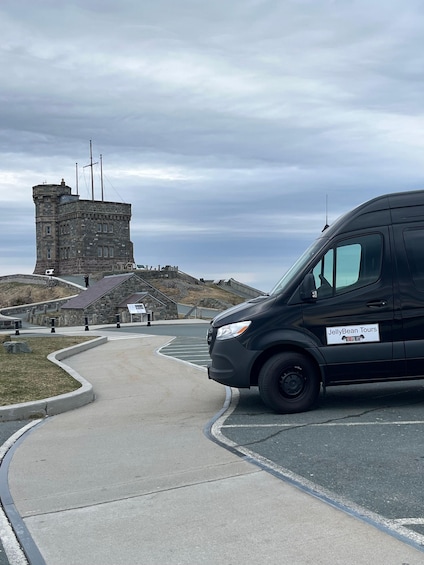 A black van with a sign reading 'JellyBean Tours' parked in front of a stone tower with a flag on top. 3