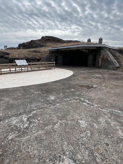 A concrete structure with a ramp leading to a tunnel entrance, surrounded by rocky terrain and a cloudy sky. 4