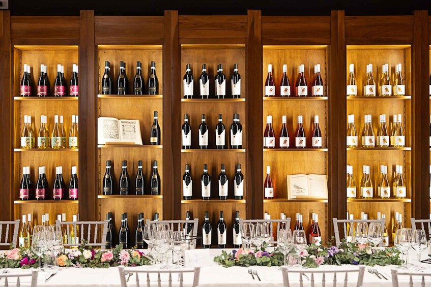 A wine cellar with shelves of wine bottles and glasses on tables. 2