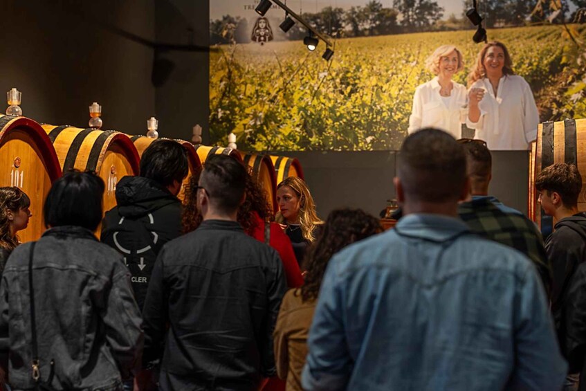 A crowd of people in a room with wooden barrels and a mural of a field. 3