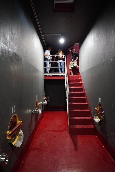 A narrow corridor with red carpet flooring, metal handrails, and a staircase leading upwards. 4