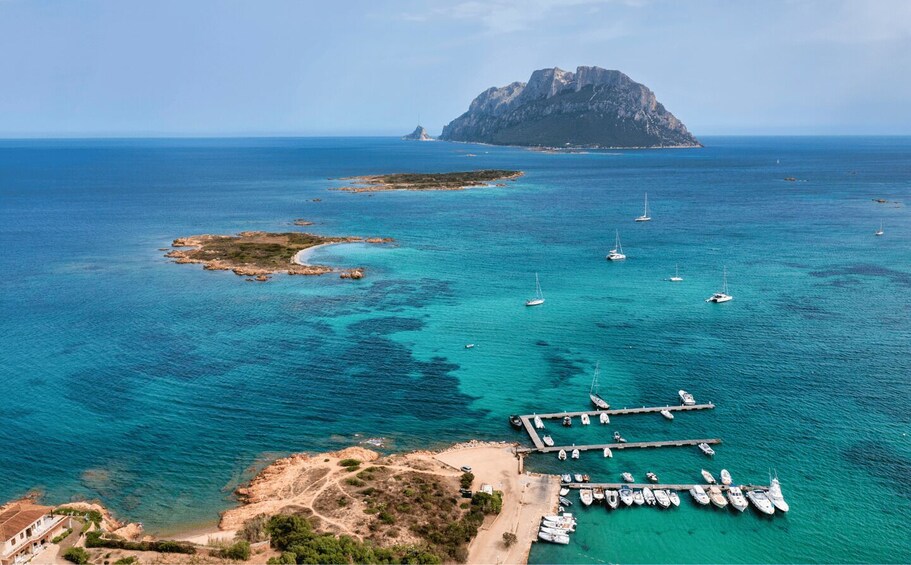 A coastal area with clear turquoise waters, a rocky island, and a marina with boats. 2