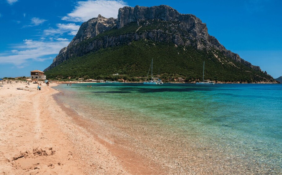 A beach with clear turquoise water, a rocky mountain, and a few boats. 5