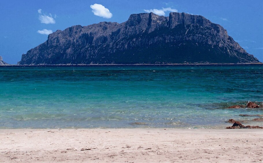A beach with clear turquoise water and a large rocky mountain in the background. 3