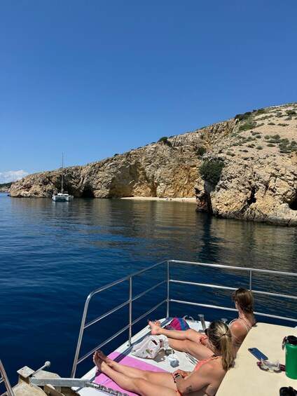 A boat with people sunbathing on the deck, rocky cliffs, and calm water. 5