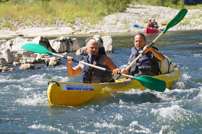 Two people kayaking on a river with rocks and other kayakers in the background. 2