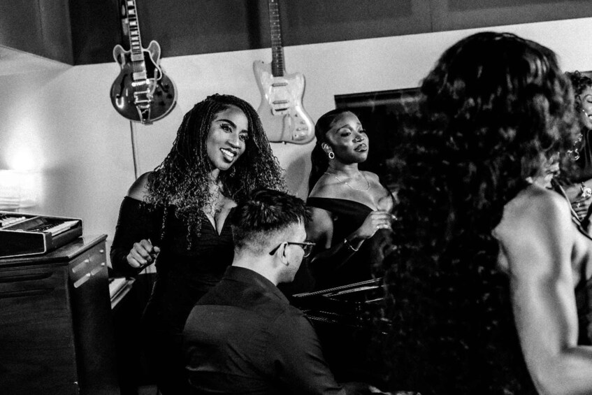 A group of people in a dimly lit room with guitars hanging on the wall. 3