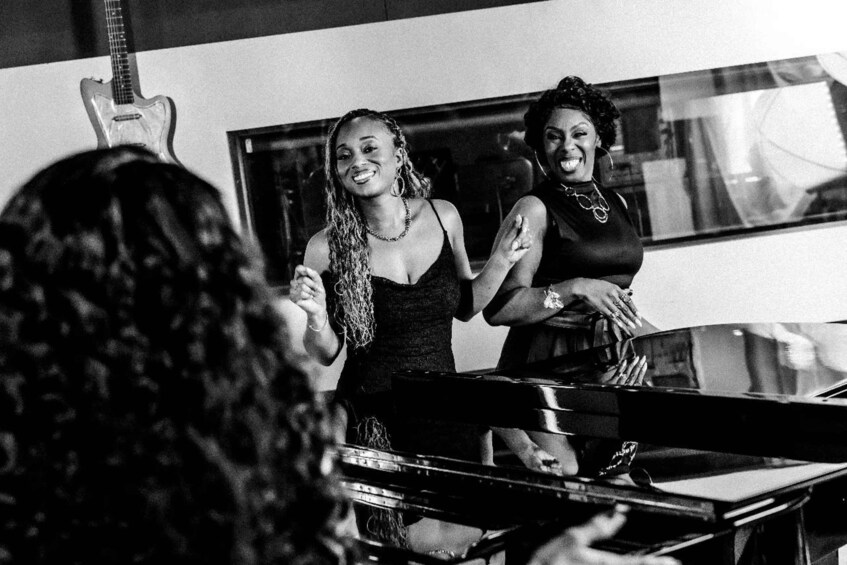 Two women standing near a piano, one playing it. 2