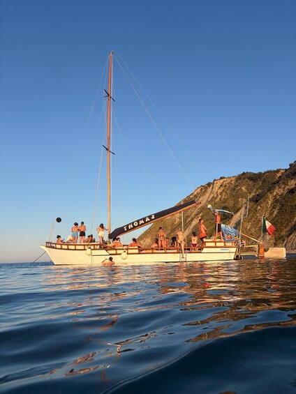 A sailboat named 'THOMAS' with people on board, anchored near a rocky coastline. 3