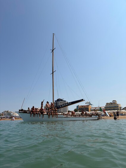 A sailboat named 'THOMAS' with people on board, docked near a beach with buildings in the background. 1