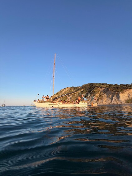 A sailboat named 'THOMAS' with people on board, sailing near a rocky coastline. 2