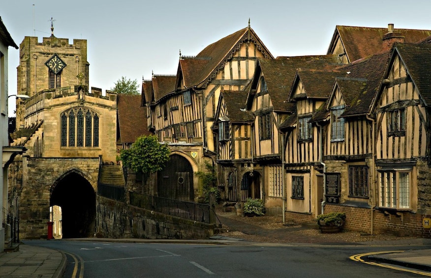 A historic town with Tudor-style buildings, a church tower, and a stone archway. 1