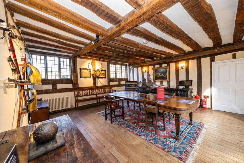 A rustic room with wooden beams, a large table, benches, and a ship model. 4