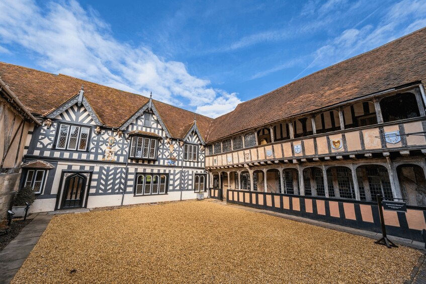 A courtyard with a cobblestone ground, a building with timber framing and a tiled roof, and a clear blue sky. 2