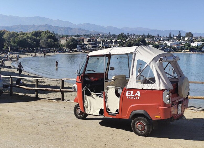 A red and white auto-rickshaw parked by a beach with mountains in the background. 4