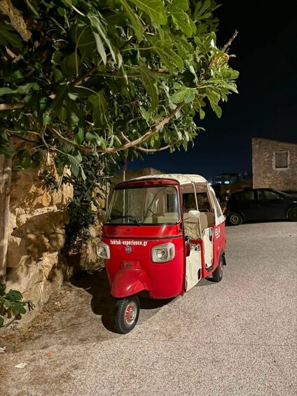 A red and white tuk-tuk parked on a street with a stone wall and a tree on the left. 3