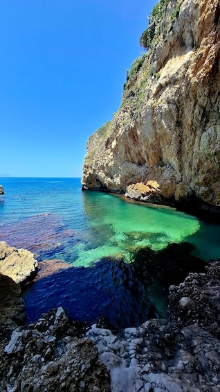 A coastal landscape with clear turquoise waters, rocky cliffs, and a clear blue sky. 1
