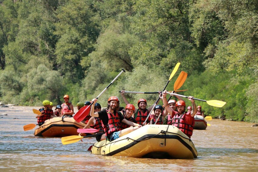 A group of people in inflatable rafts on a river, wearing life jackets and helmets, paddling with oars. 2