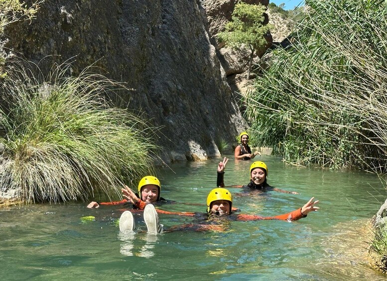 People in water with helmets, surrounded by rocky cliffs and vegetation. 1