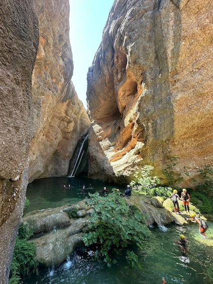 A canyon with a waterfall, people swimming, and a small stream. 5