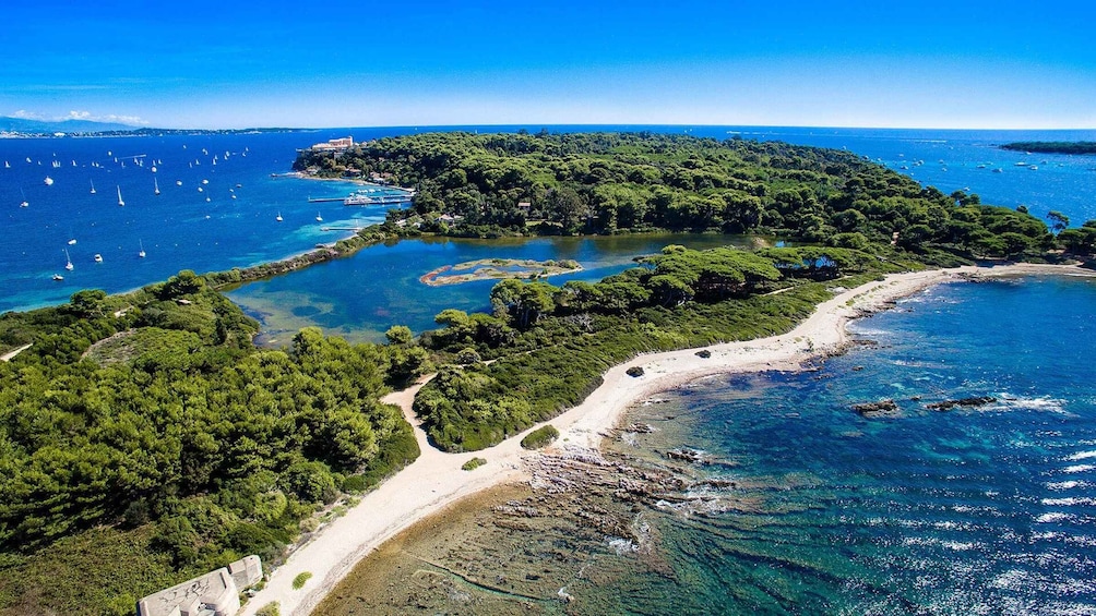A coastal landscape with a sandy beach, a forested island, and clear blue waters with sailboats. 1