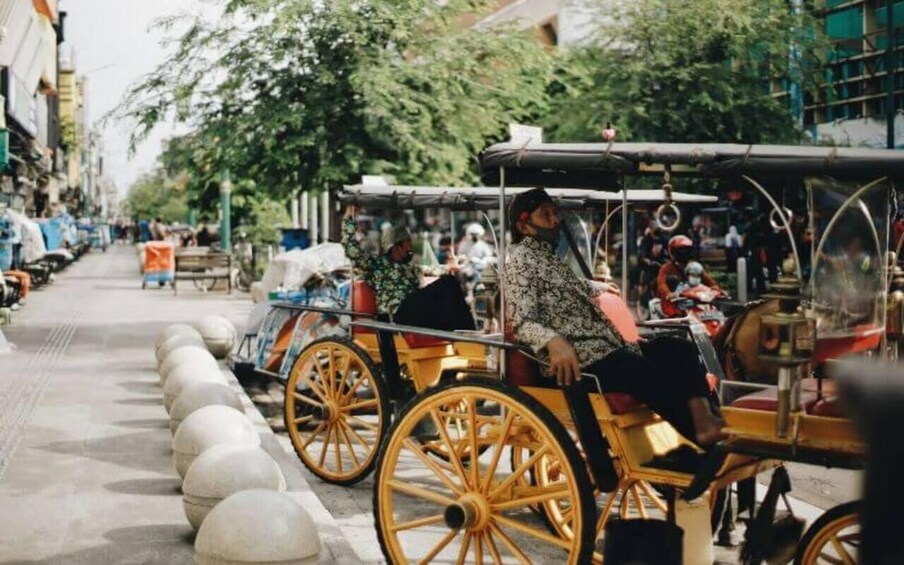 A street with a yellow horse-drawn carriage, a person riding it, and a row of white bollards along the sidewalk. 2