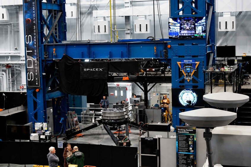 A space simulation facility with a large blue structure labeled 'SPACEX' and a docking system capabilities sign. 3