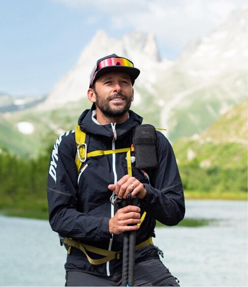 A person wearing a helmet and harness, holding a rope, with a mountainous landscape in the background. 4