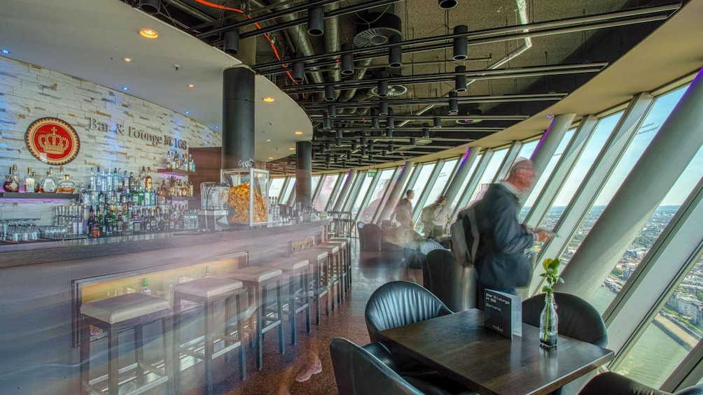 A modern bar with a high ceiling, exposed pipes, and a city view through large windows. 3