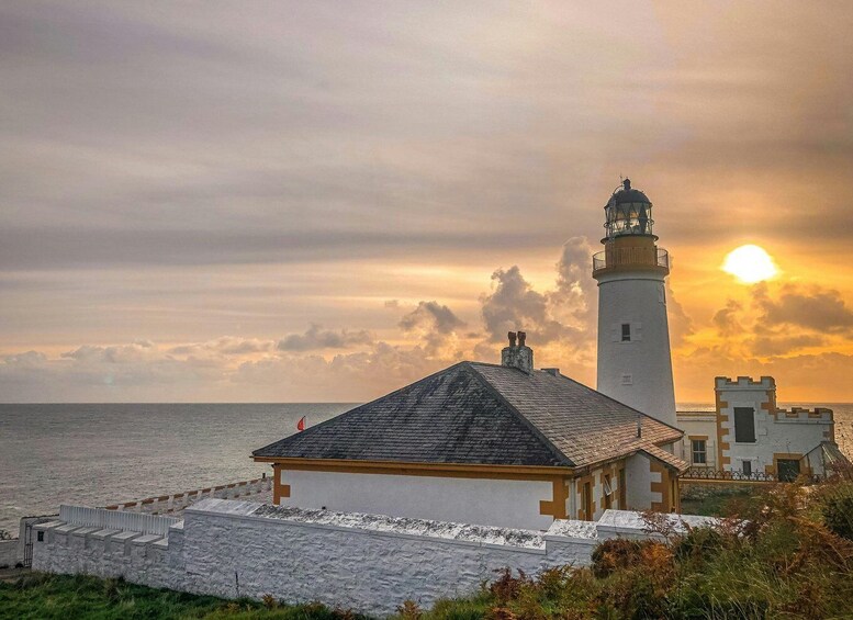 A lighthouse, a white building, and a sunset over the ocean. 3