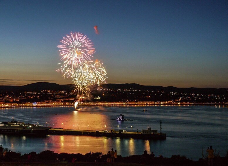 A nighttime cityscape with a large fireworks display over a body of water. 1