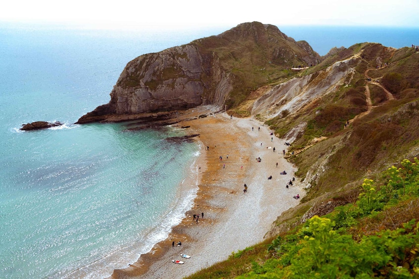 A coastal landscape with a rocky cliff, a sandy beach, and a clear view of the ocean. 2