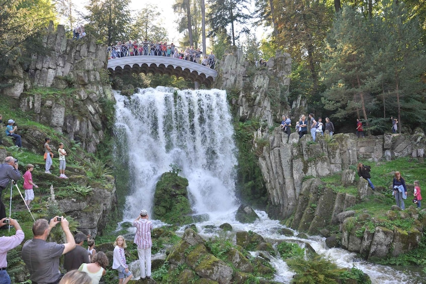 A waterfall with a viewing platform above it, surrounded by lush greenery. 4