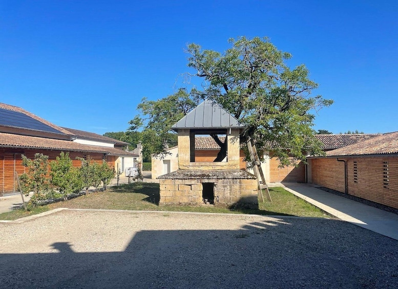 A courtyard with a stone structure, a tree, and buildings with tiled roofs. 1