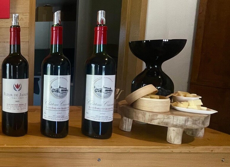 Three bottles of Saint-Emilion Grand Cru wine from 2017, a wooden wine rack, and a bowl of cheese. 5