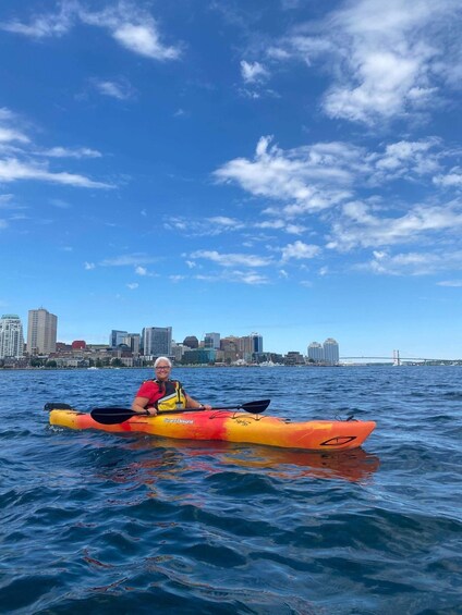 A person kayaking on a body of water with a city skyline in the background. 1