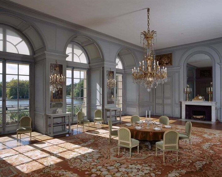 A grand dining room with a large chandelier, ornate chairs, and a patterned carpet. 4