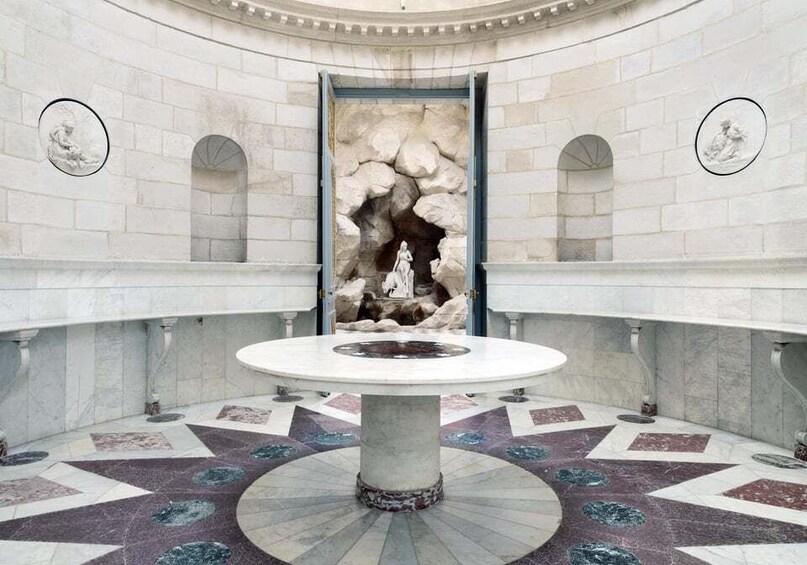 A circular room with a central fountain, stone walls, and a patterned floor. 5